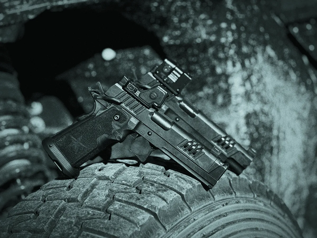 Handgun with a red dot sight and compensator resting on an off-road tire